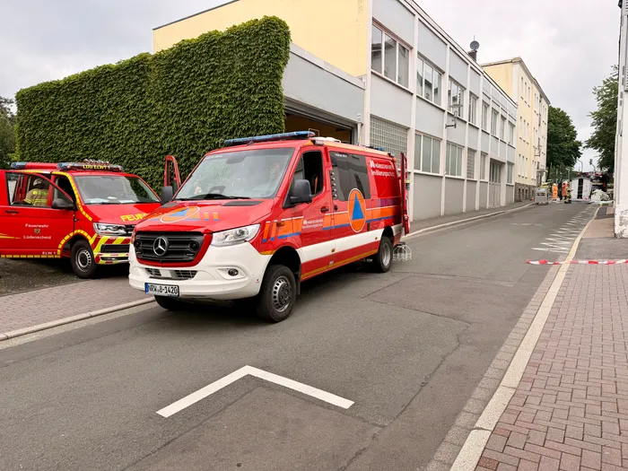 Zwei rote Rettungswagen mit Blaulicht stehen vor einem hellen Gebäude mit einer großen Toröffnung. Im Vordergrund ist ein Pfeil auf dem Asphalt zu sehen.