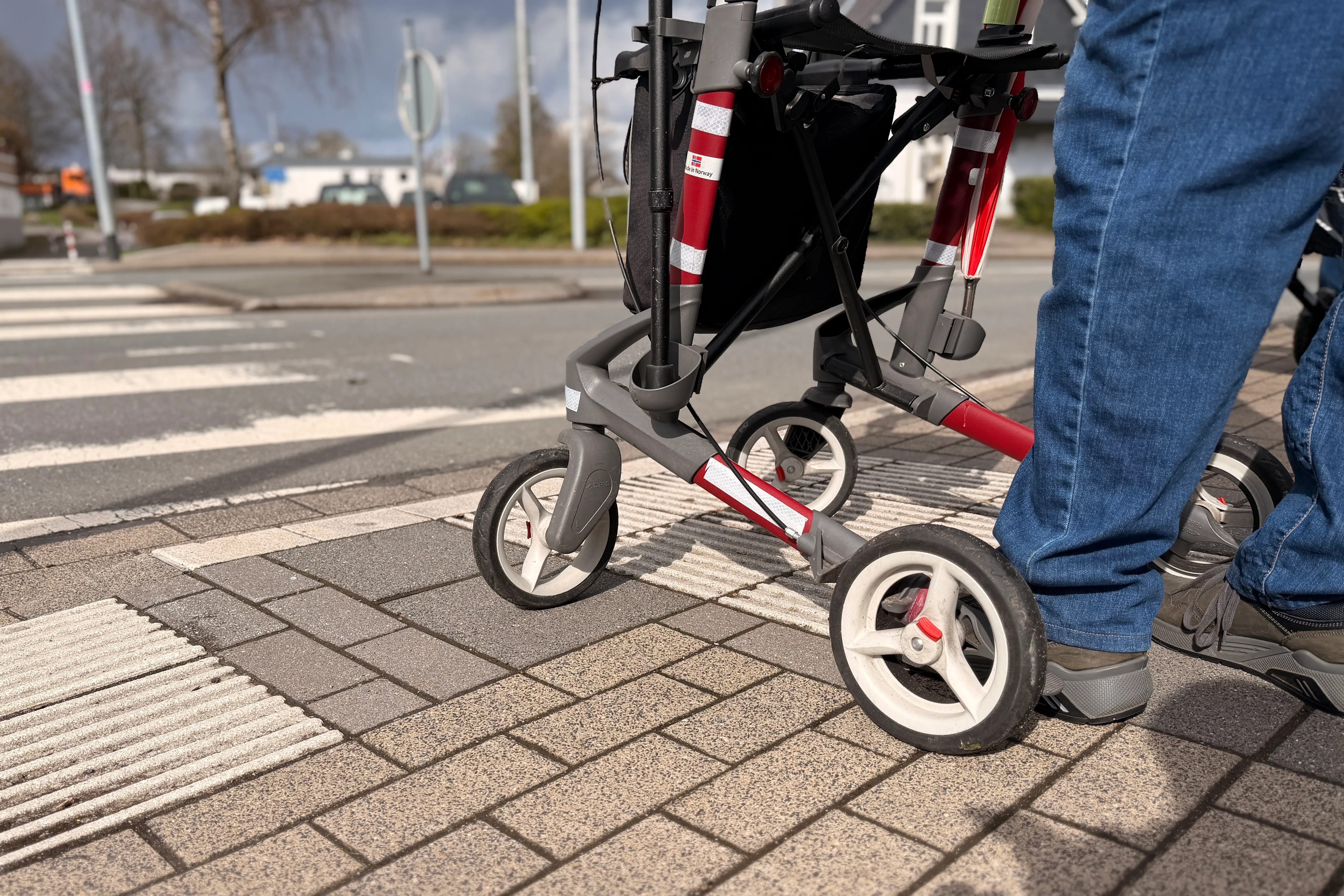 Ein Rollator überquert einen Zebrastreifen, dessen Anfang durch taktile Leitelemente für sehbehinderte Menschen markiert ist.