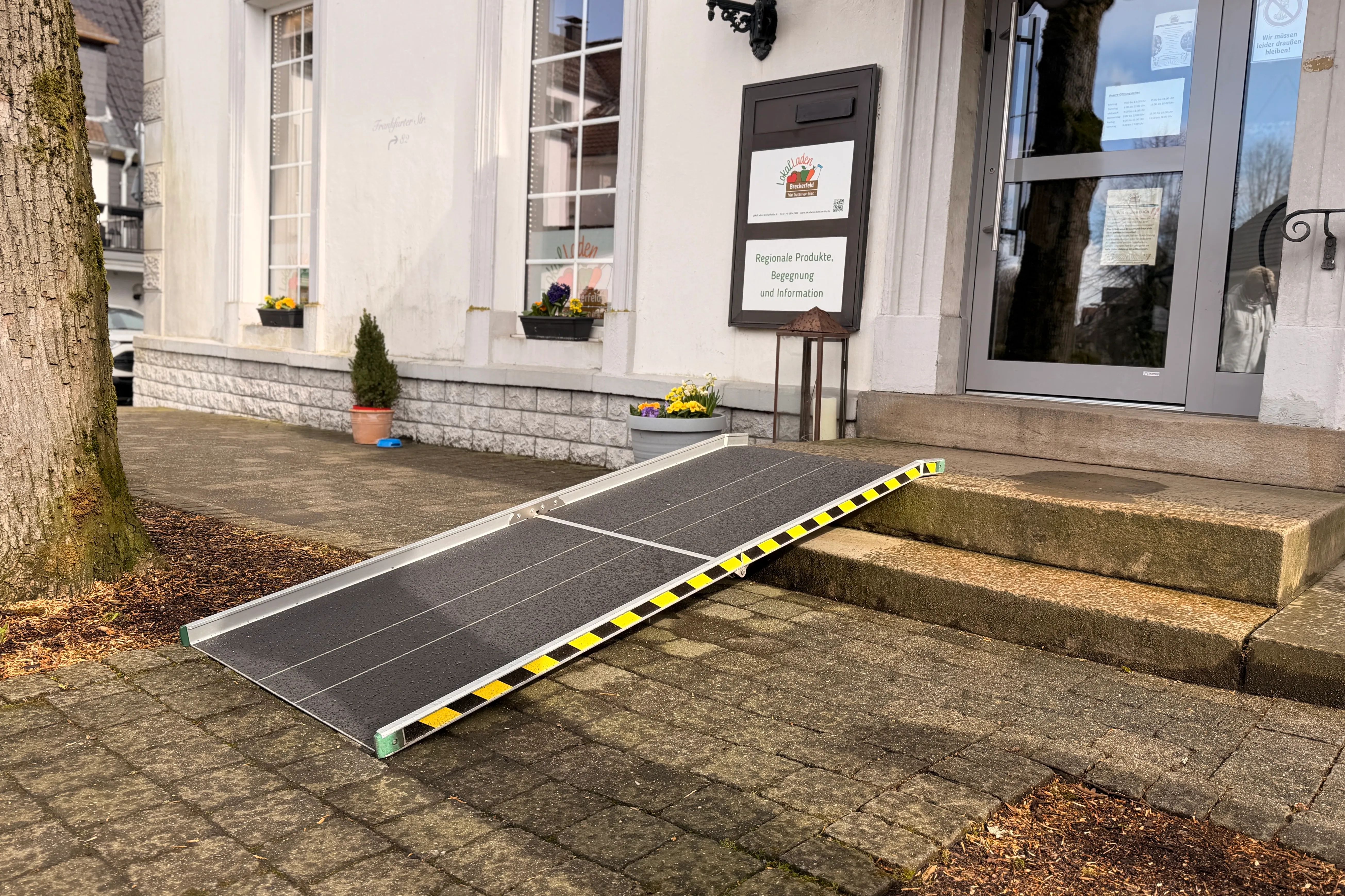 Eine mobile Rampe führt zur Eingangstür eines Geschäfts mit dem Schild „Regionale Produkte, Begegnung und Information“.