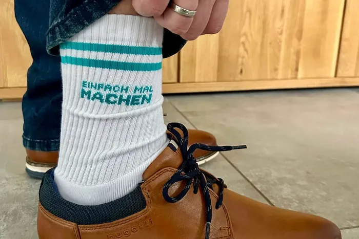 Nahaufnahme von Füßen mit Socken und Schuhen. Auf der Socke steht in grüner Schrift: „EINFACH MAL MACHEN“.