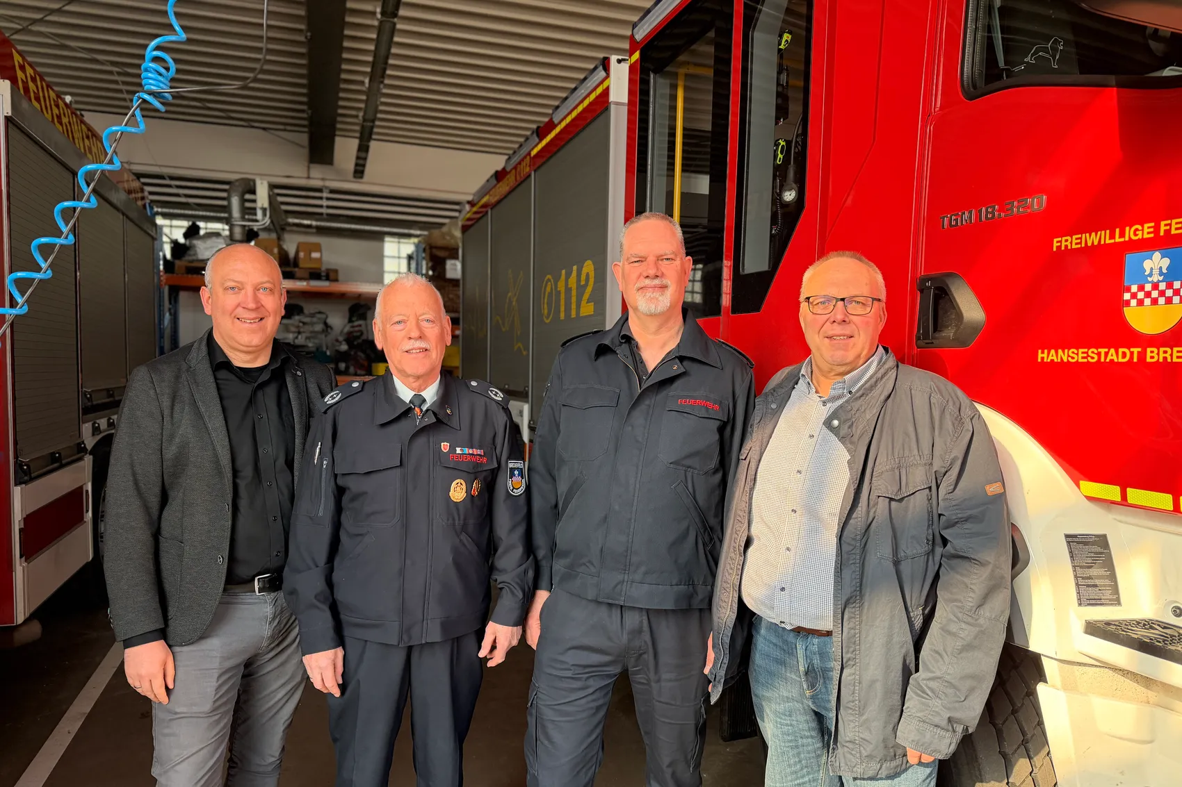 Vier Männer posieren vor einem roten Feuerwehrauto. Von links: Bürgermeister André Dahlhaus im Anzug, Norbert Lohoff und Dirk Neuhaus in Feuerwehruniformen, Andreas Bleck mit Jacke.