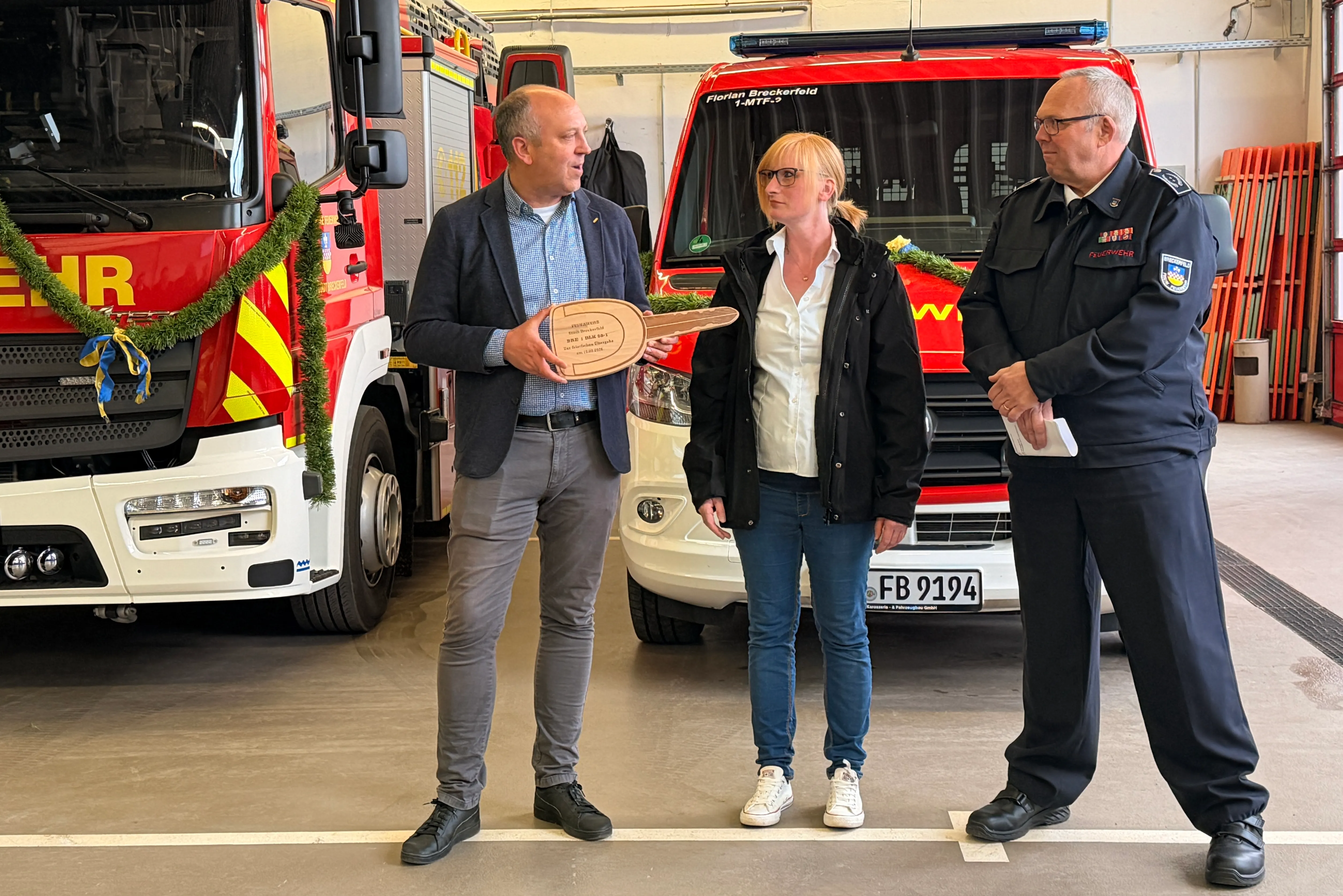 Bürgermeister André Dahlhaus überreicht Wehrleiter Andreas Bleck einen symbolischen Schlüssel, während Miriam Link von Magirus daneben steht. Im Hintergrund ein rotes Feuerwehrfahrzeug.