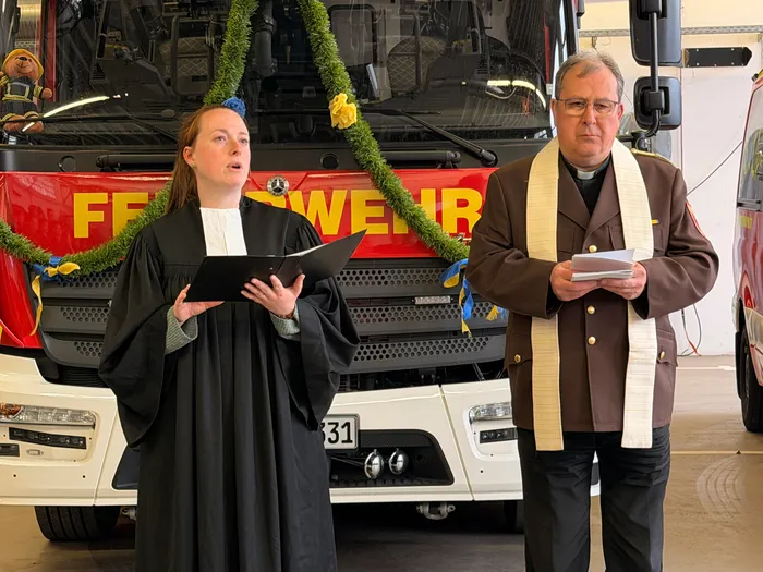 Pfarrerin und Pater sprechen vor einem Feuerwehrauto einen Segen für die Feuerwehrleute und deren neue Fahrzeuge.