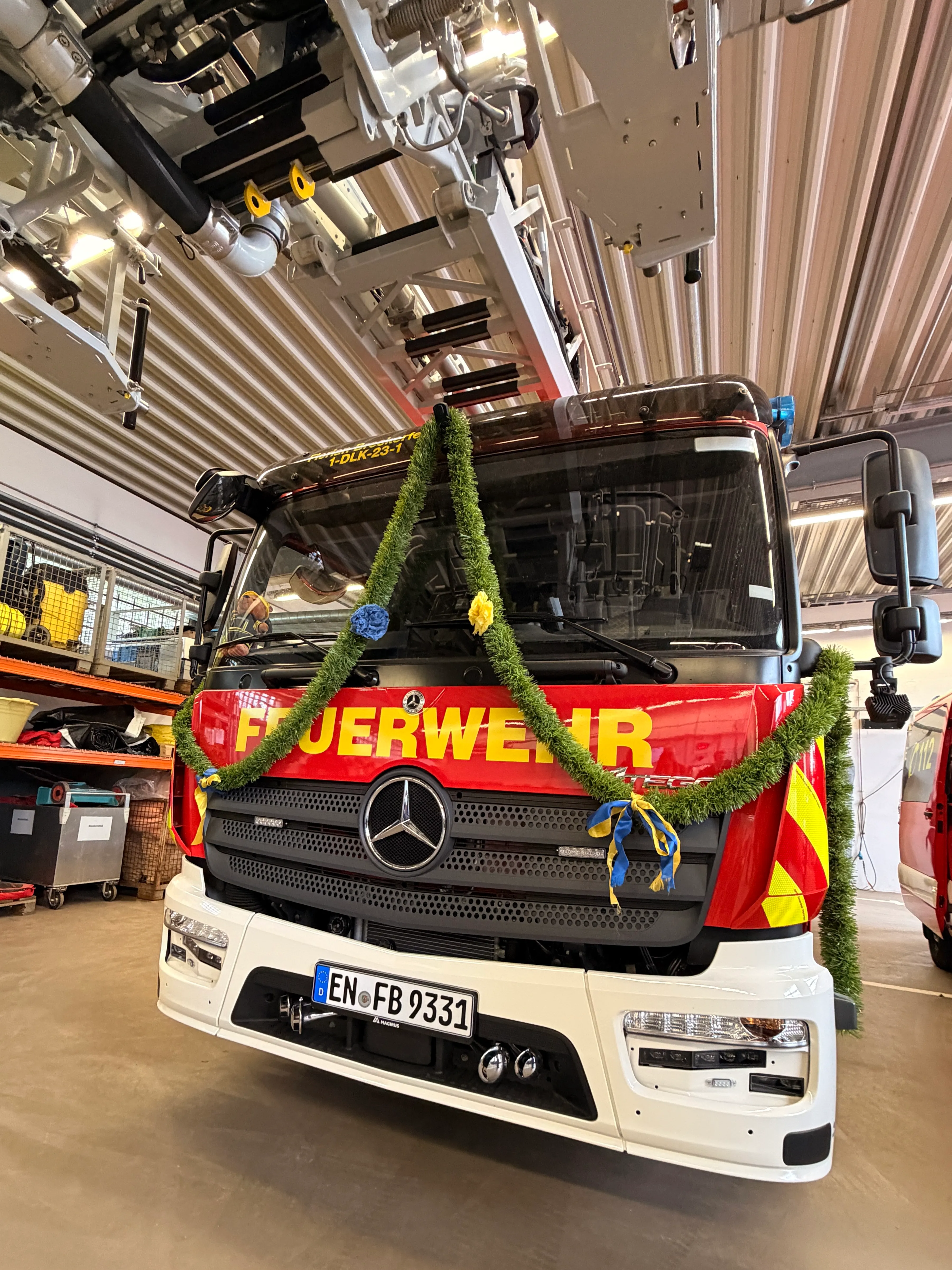Rot-gelbes Feuerwehrauto der Marke Mercedes-Benz mit dem Kennzeichen EN FB 9331, geschmückt mit Tannenzweigen und Bändern.