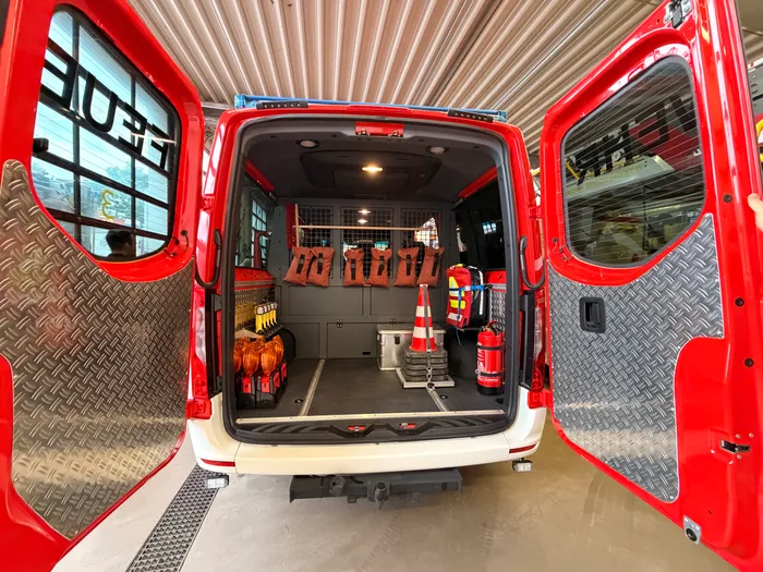 Innenraum eines geöffneten roten Mannschaftstransportwagens der Feuerwehr mit Ausrüstung wie Warnwesten, Kanistern und Verkehrskegeln.