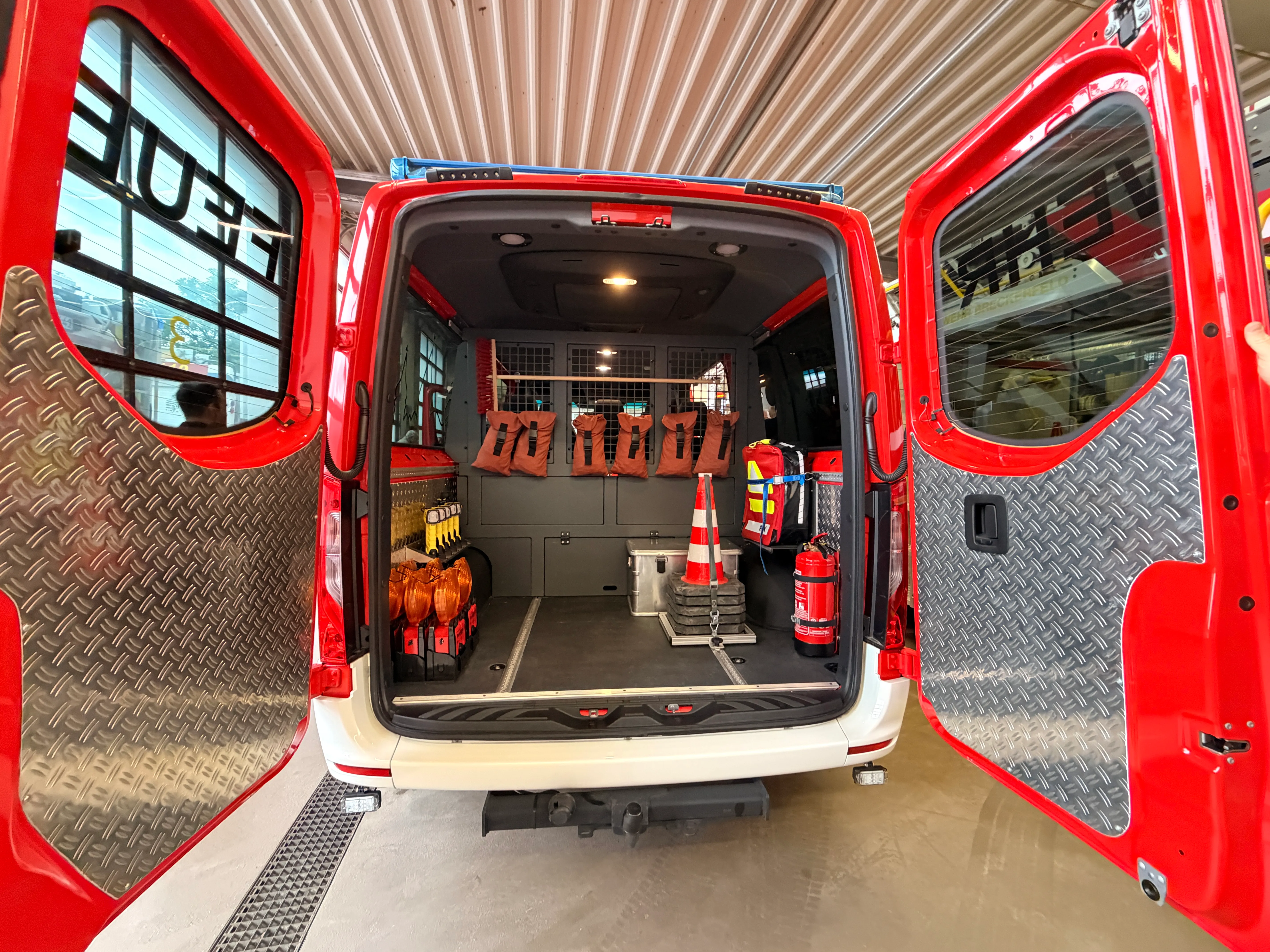 Innenraum eines geöffneten roten Mannschaftstransportwagens der Feuerwehr mit Ausrüstung wie Warnwesten, Kanistern und Verkehrskegeln.