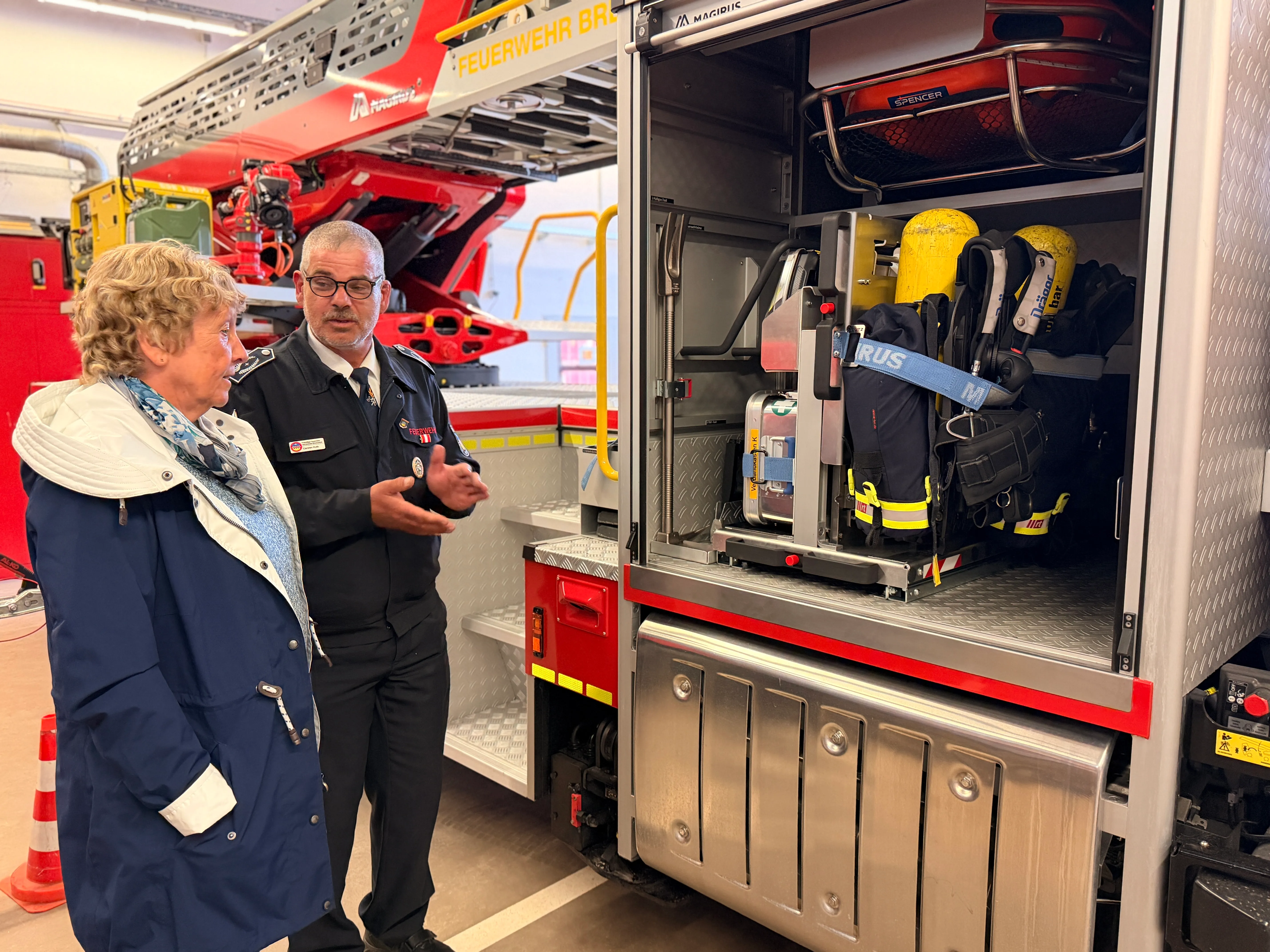 Feuerwehrmann erklärt einer Frau die Ausrüstung an einem geöffneten Schrank des neuen Einsatzfahrzeugs.