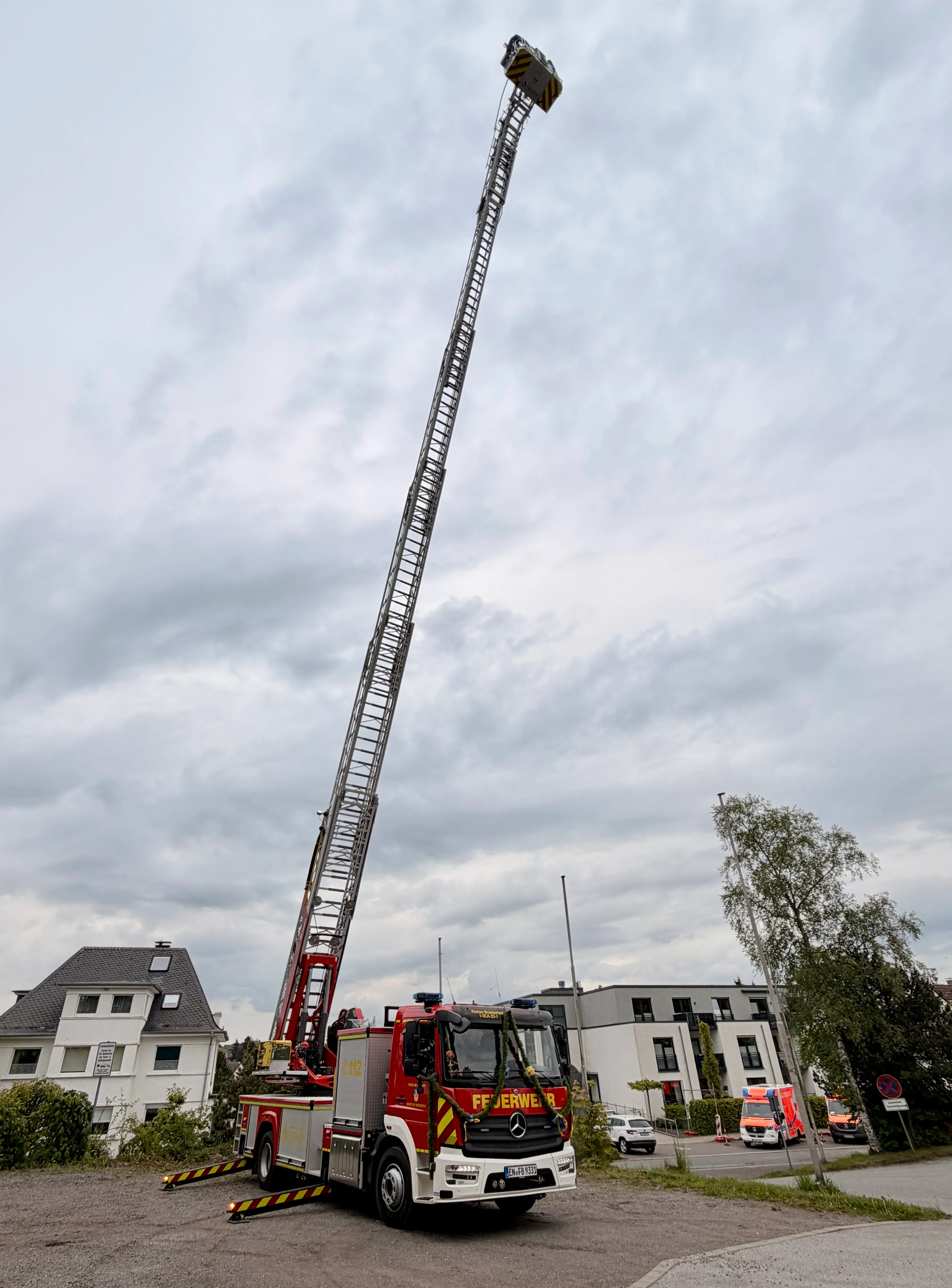 Roter Feuerwehrauto mit ausgefahrenem Teleskoparm vor Wohngebäuden an bewölktem Tag.