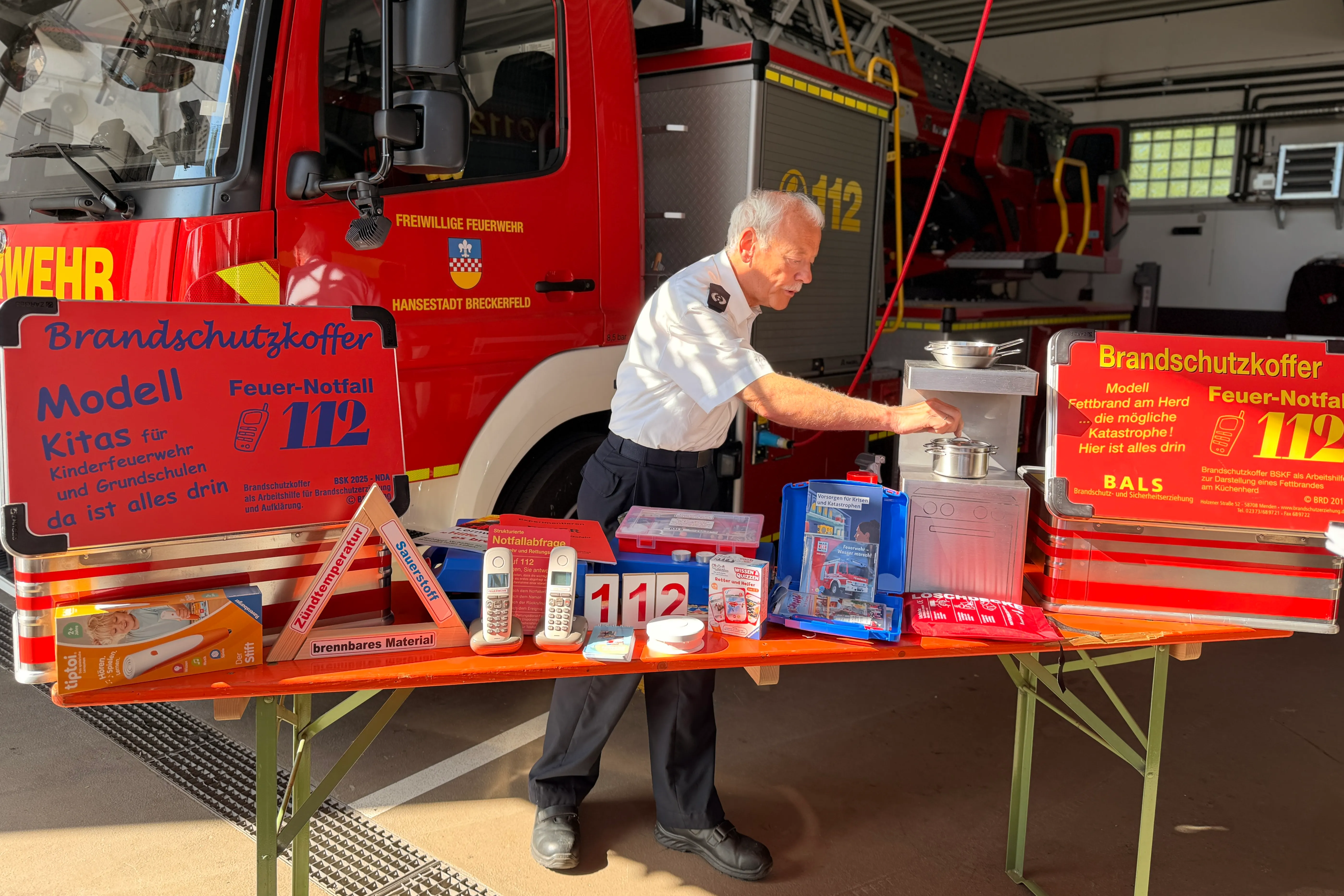 Zwei Feuerwehrleute demonstrieren den Inhalt eines Brandkoffers für Kindergärten und Grundschulen, der unter anderem Verbandsmaterial, eine Schere und eine Rettungsdecke enthält.