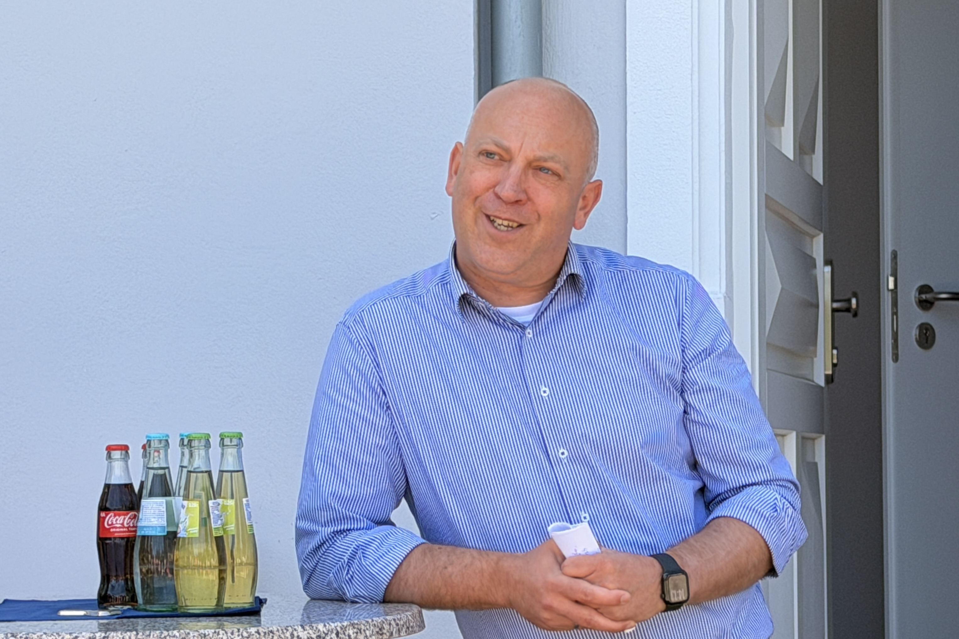 Bürgermeister André Dahlhaus lächelt in die Kamera, neben ihm stehen Flaschen mit Erfrischungsgetränken auf einer Ablage.
