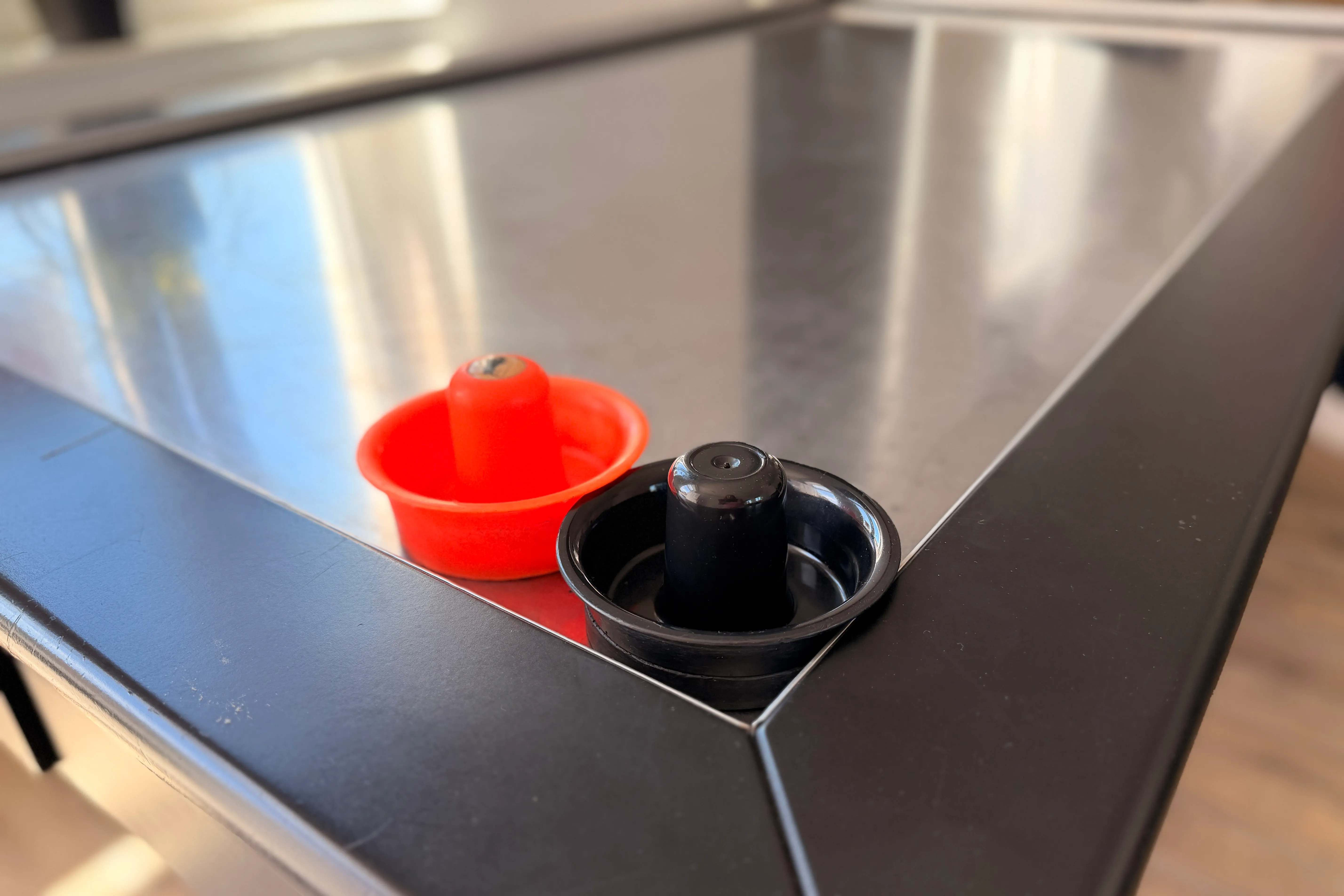 Zwei Spielsteine für Airhockey, rot und schwarz, stehen auf der glänzenden Spieloberfläche einer Airhockey-Platte.