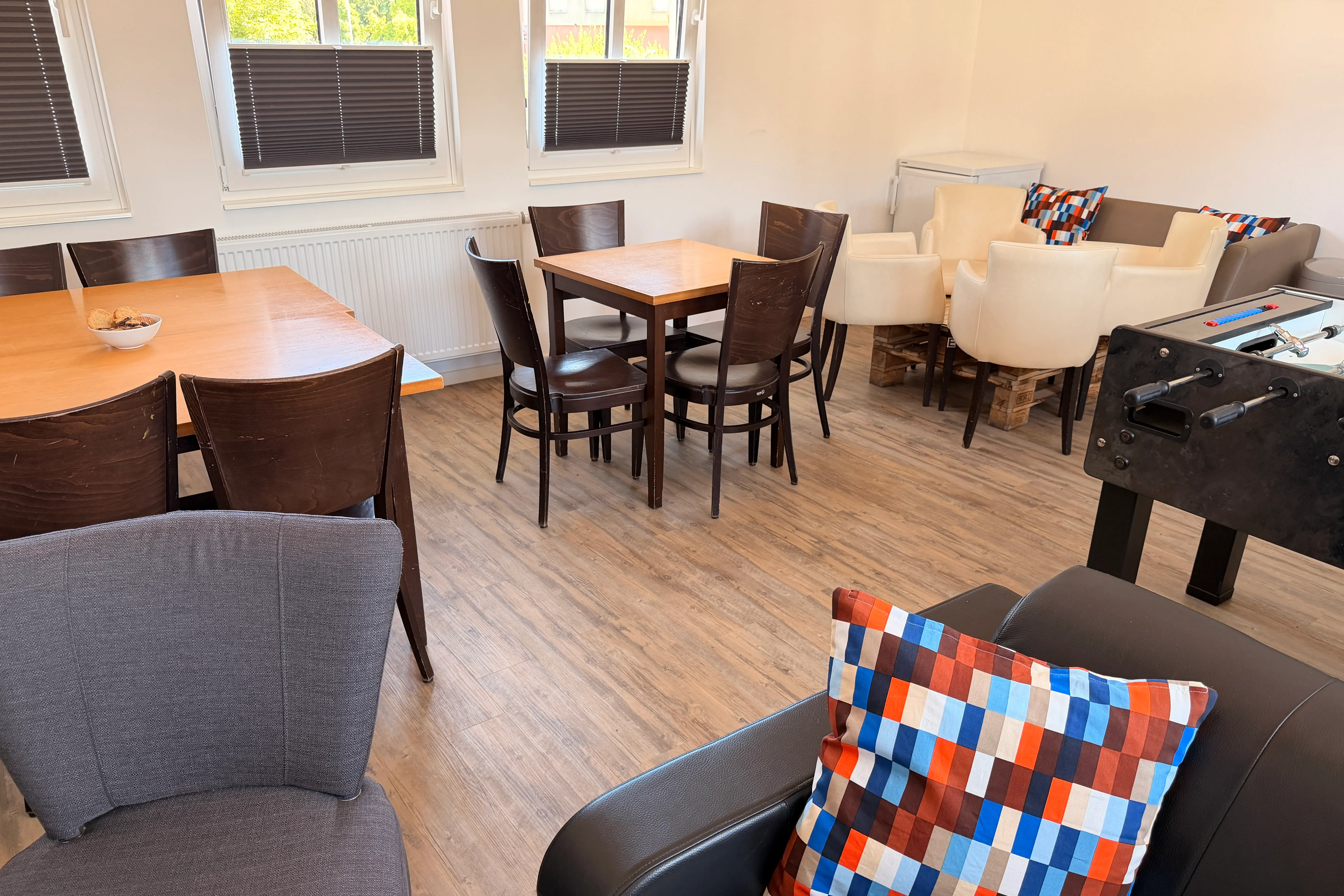 Ein helles, freundliches Jugendzentrum mit Tischen, Stühlen, Sofas und einem Tischfußballspiel.