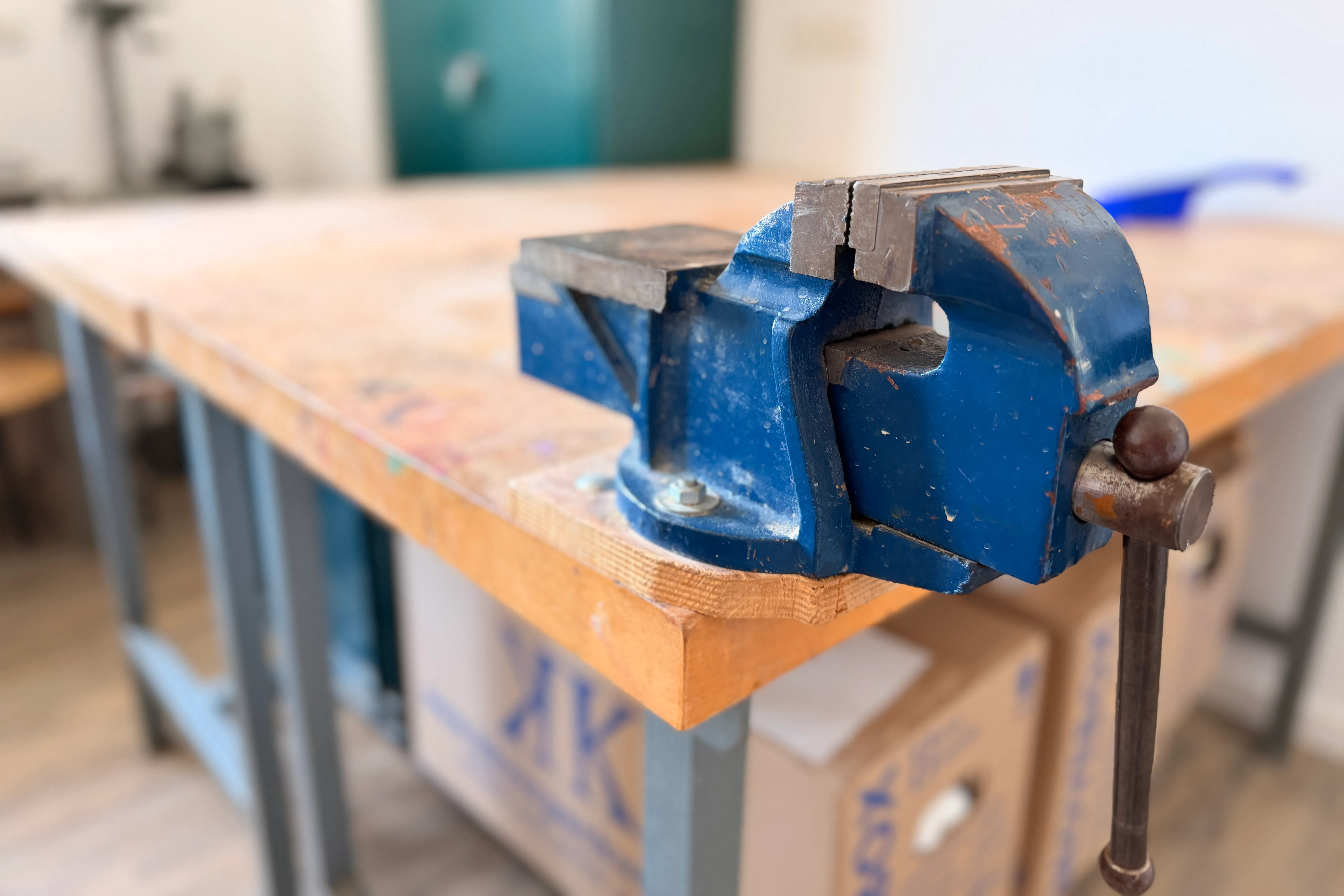Eine blaue Schraubstock ist auf einem Holztisch in einem hellen Raum montiert.