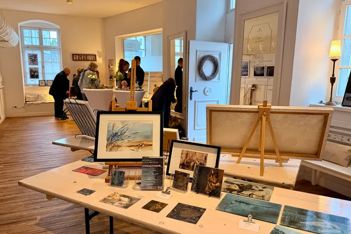 Ausstellungsstücke und Besucher bei der Museumsnacht. Auf einem Tisch sind Gemälde, Drucke und Karten ausgestellt, im Hintergrund stehen Menschen in einem hellen Raum mit hohen Decken und Türen.