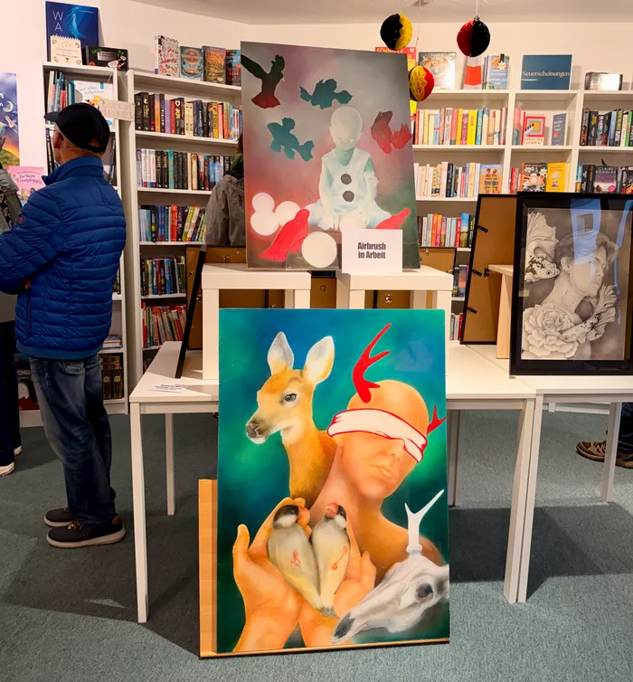 Ein Mann betrachtet ein großes, farbenfrohes Gemälde eines Rehs mit einem kleinen Vogel auf den Händen in einer Buchhandlung während der Museumsnacht. Im Hintergrund sind weitere Kunstwerke und Bücherregale zu sehen.