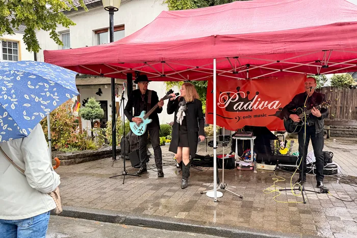 Eine Band spielt unter einem roten Zelt bei der Museumsnacht in Breckerfeld. Ein Gitarrist, eine Sängerin und ein weiterer Musiker mit Gitarre sind zu sehen.