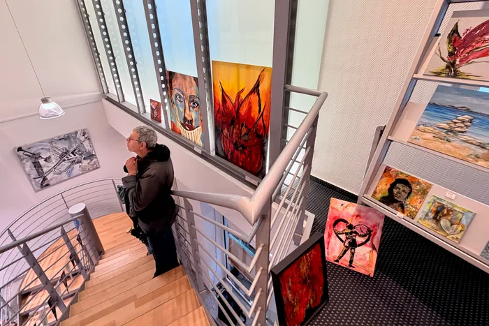 Ein Mann betrachtet Gemälde an einer Treppe in einer hellen Galerie während der Museumsnacht. Verschiedene Kunstwerke sind an den Wänden und auf dem Boden ausgestellt.