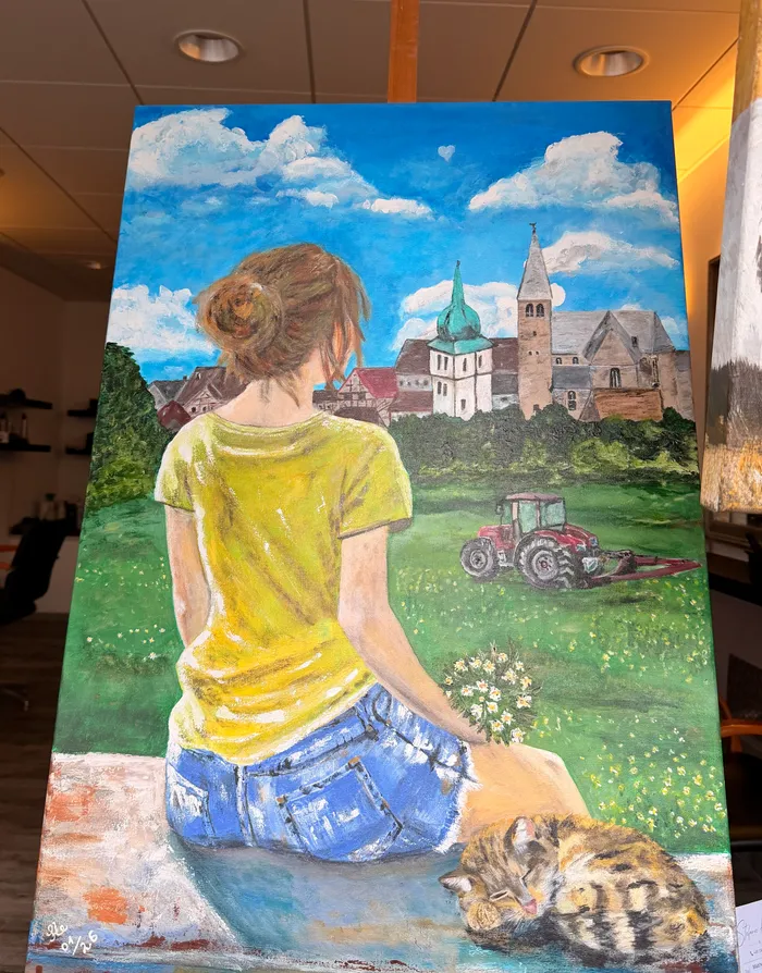 Eine Frau mit hochgestecktem, braunem Haar sitzt einem alten Gemäuer mit Kirchturm und rotem Traktor zugewandt. Vor ihr liegt eine Katze auf einer Wiese mit Blumen.