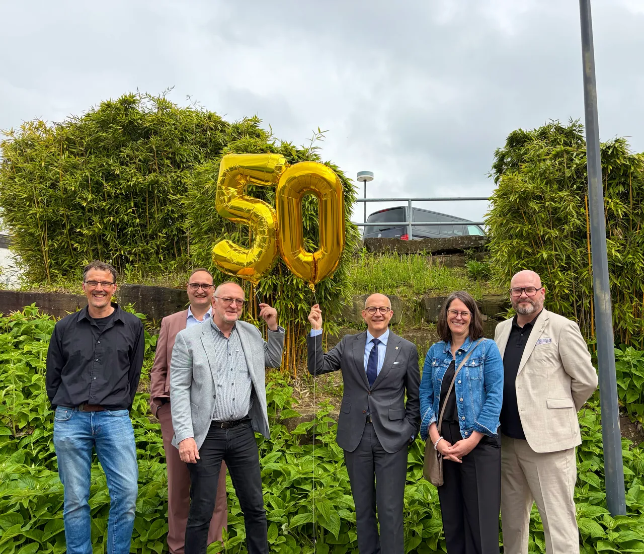 Sechs Personen stehen vor einem grünen Hintergrund mit der goldenen Zahl „50“. Landrat Ralf Schwarzkopf hält die Zahl hoch.