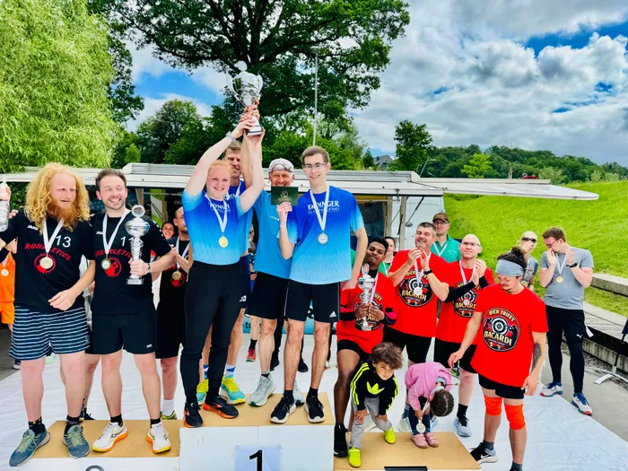 Sieger der 4. Biathlonstaffel-Challenge stehen auf dem Podium, halten Pokale und Medaillen hoch. Ein Kind steht vor der Gruppe und blickt nach oben.