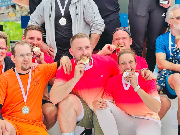 Mehrere Sportler posieren mit Medaillen, darunter zwei mit Goldmedaillen, nach der 4. Biathlonstaffel-Challenge an der Volme. Die Sportler tragen Trikots in Orange und Rot und lächeln in die Kamera.