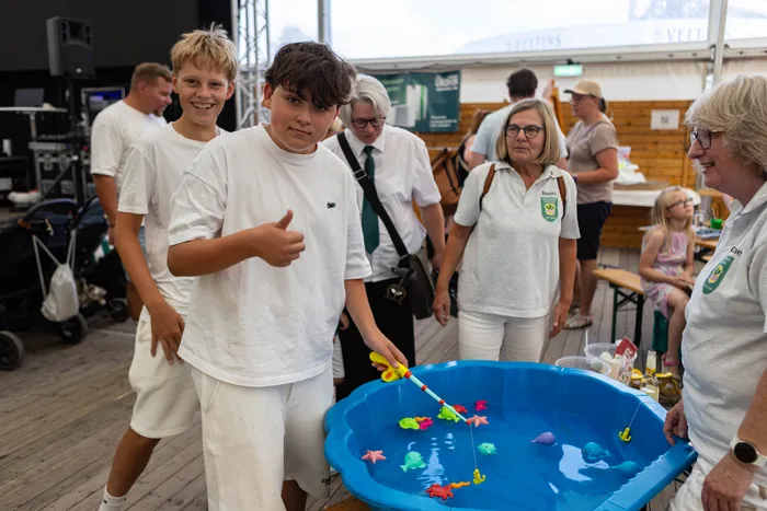 Ein Junge in weißem T-Shirt gibt einen Daumen nach oben neben einem blauen Planschbecken mit bunten Spielzeugfischen.