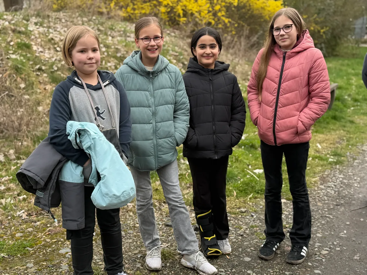 Vier Mädchen stehen nebeneinander im Freien, lächeln in die Kamera. Sie tragen Winterjacken und Jeans.