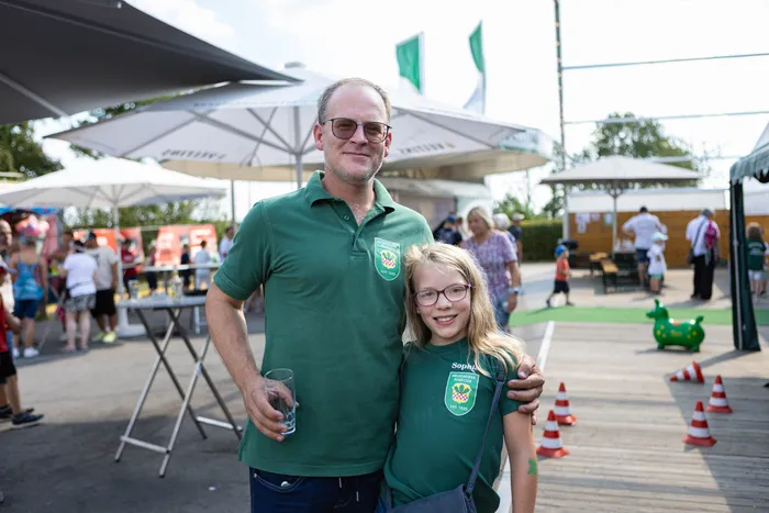 Ein Mann und ein Mädchen in grünen Poloshirts mit Vereinswappen lächeln bei einem Schützenfest.