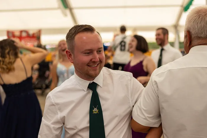 Ein lächelnder Mann in weißem Hemd und grüner Krawatte feiert im Festzelt beim Schützenfest.