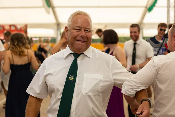 Ein lächelnder Mann in weißem Hemd und grüner Krawatte bei einem Schützenfest.