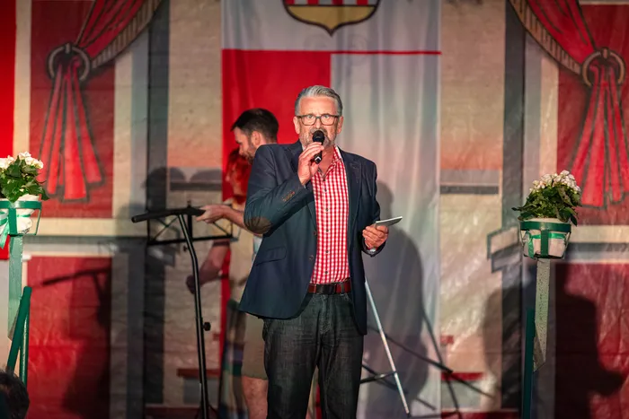 Ein Mann mit Brille und blauem Sakko spricht in ein Mikrofon auf einer Bühne beim Schützenfest.