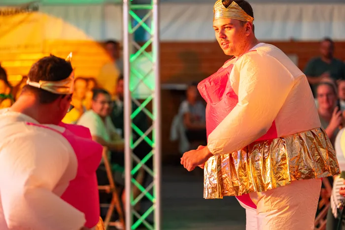 Zwei Personen in weiß-rosa Kostümen mit goldenen Akzenten stehen vor einer Zuschauermenge bei einem Schützenfest.