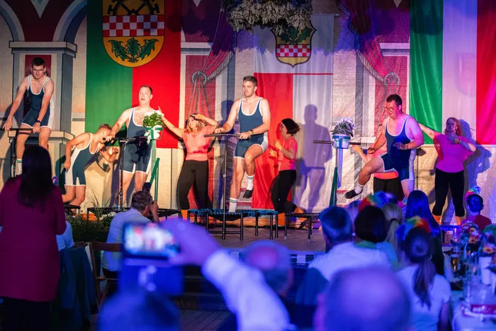 Männer in blauen Sportanzügen und Frauen in rosa T-Shirts führen eine Aufführung auf einer Bühne während des Schützenfestes auf.