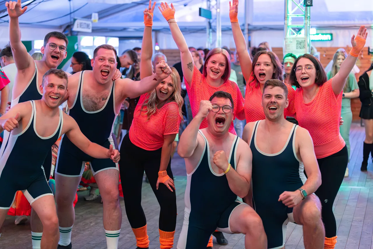 Eine Gruppe jubelnder Menschen in dunklen Singlets und pinken Mesh-Oberteilen feiert beim Schützenfest.