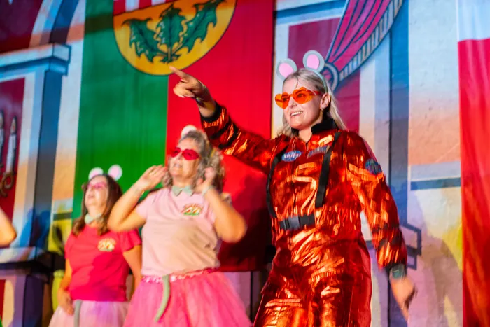 Frauen in bunten Kostümen, Sonnenbrillen und Mäuseohren stehen auf einer farbenfrohen Bühne während des Schützenfestes.