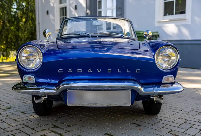 Frontansicht eines blauen Caravelle-Cabriolets mit Chromstoßstange auf einem gepflasterten Platz.