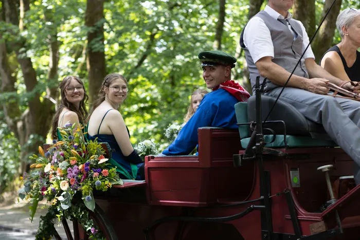 Auf einem roten Pferdewagen sitzen lächelnd der neue Schützenprinz in Uniform und drei weitere Personen, während sie durch einen Wald fahren.