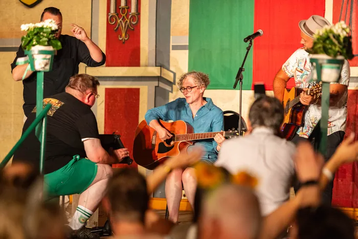 Musiker spielen Gitarre auf einer Bühne mit farbenfrohem Hintergrund beim Bunten Dorfabend des Schützenfestes.