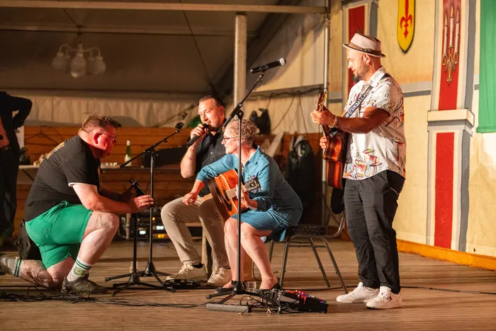 Musiker spielen Gitarre und Ukulele auf einer Bühne während eines Schützenfestes unter einem Zelt.