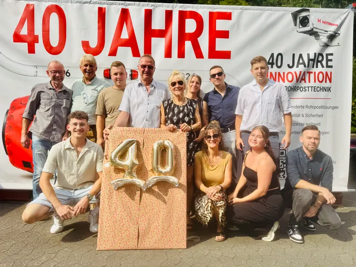 Eine Gruppe von Menschen posiert vor einem Banner zum 40-jährigen Jubiläum von Heitmann und hält eine große, dekorierte Zahl „40“.
