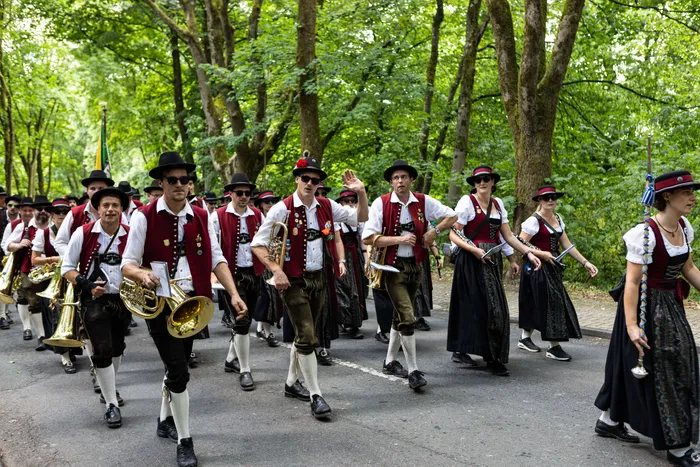 Eine Blaskapelle in Tracht marschiert auf einer Straße, während ein Schützenfest stattfindet.