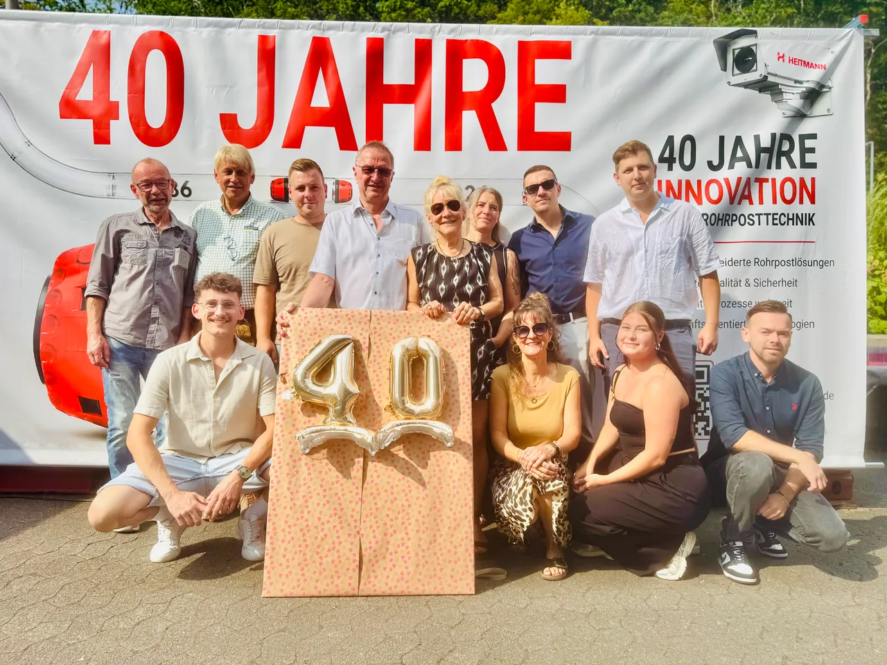 Eine Gruppe von Menschen posiert vor einem Banner zum 40-jährigen Firmenjubiläum von Heitmann und hält eine große, dekorative Zahl 40.