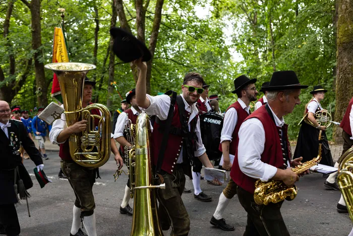 Ein Schützenfestzug mit einer Blaskapelle zieht an Zuschauern vorbei, während ein Musiker seinen Hut in die Luft wirft.