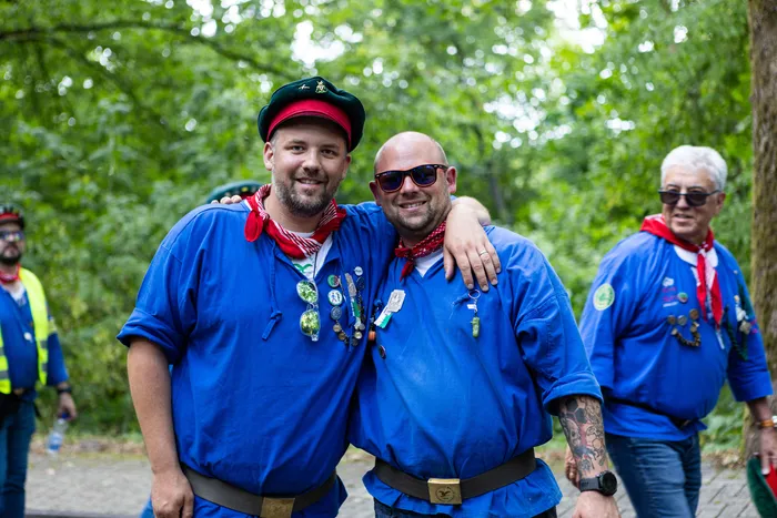 Zwei Männer in blauem Hemd und mit Schützenabzeichen umarmen sich vor Bäumen.