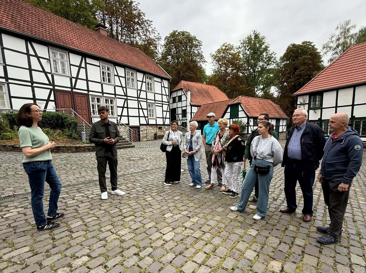 Eine Frau spricht zu einer Gruppe von Menschen in einem gepflasterten Hof vor historischen Fachwerkhäusern.