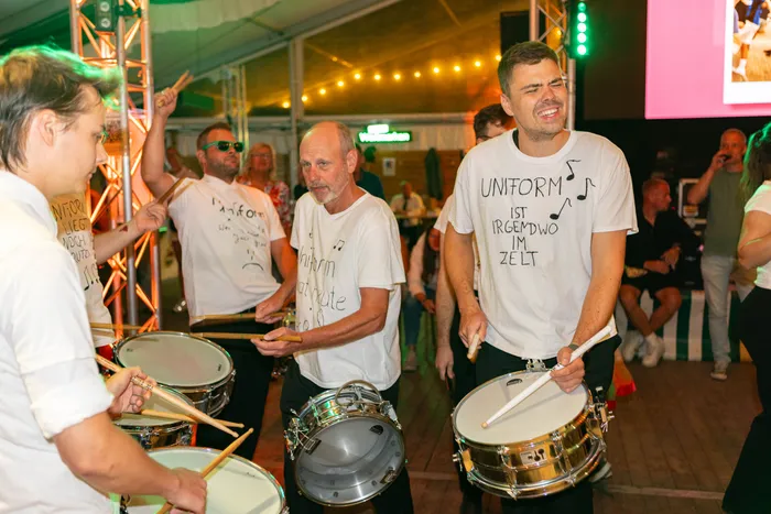 Männer in weißen T-Shirts spielen Trommeln in einem Festzelt während des Schützenfestes.