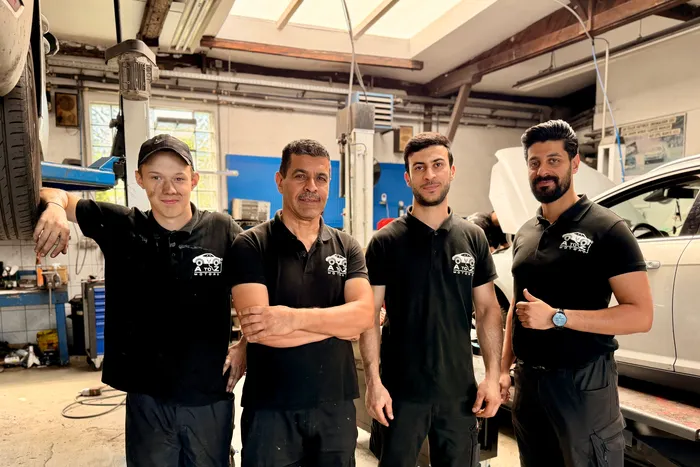 Vier Männer in schwarzen Poloshirts stehen in einer Kfz-Werkstatt.