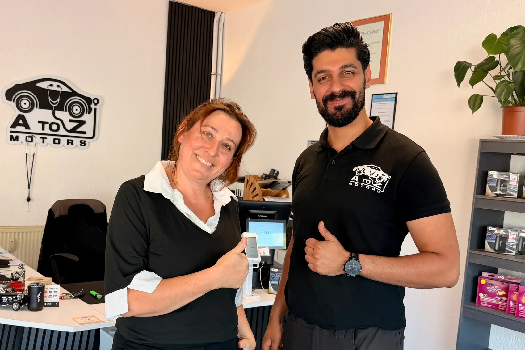 Abdullah Al-Shaikhli und Dorothea Kabeck geben in ihrem Büro bei „A to Z Motors“ jeweils einen Daumen nach oben.