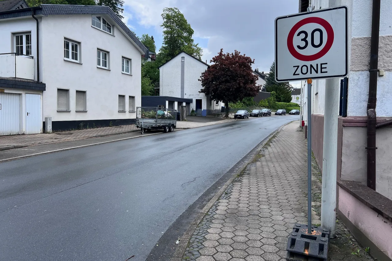 Schild „30 Zone“ am Straßenrand einer wenig befahrenen Straße in einer Wohngegend.