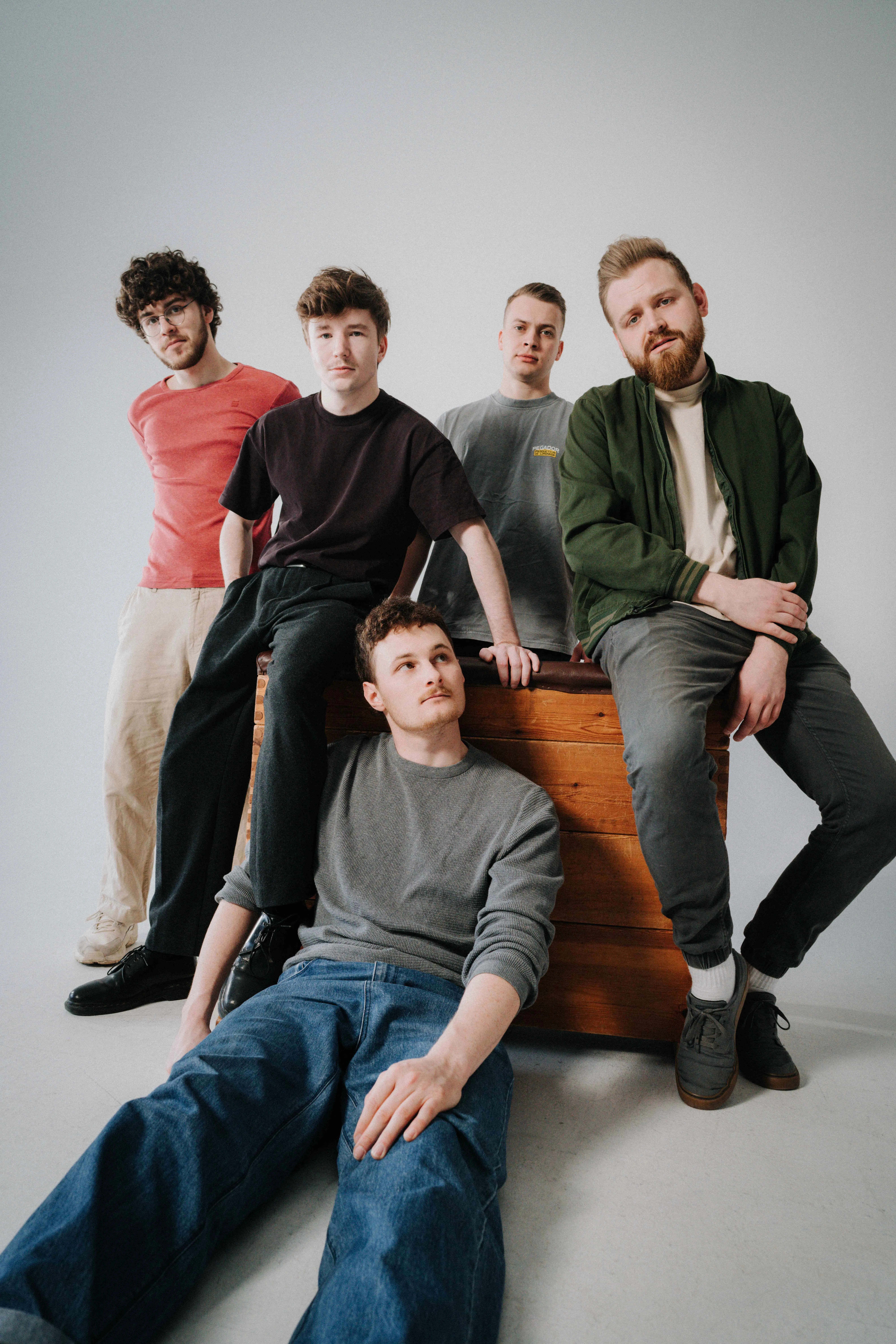 Fünf junge Männer posieren für ein Bandfoto. Sie sitzen und lehnen auf einer hölzernen Kiste, ein Mann liegt davor. Die Band 5Raumfenster spielt gitarrenlastigen Rock mit deutschen Texten.